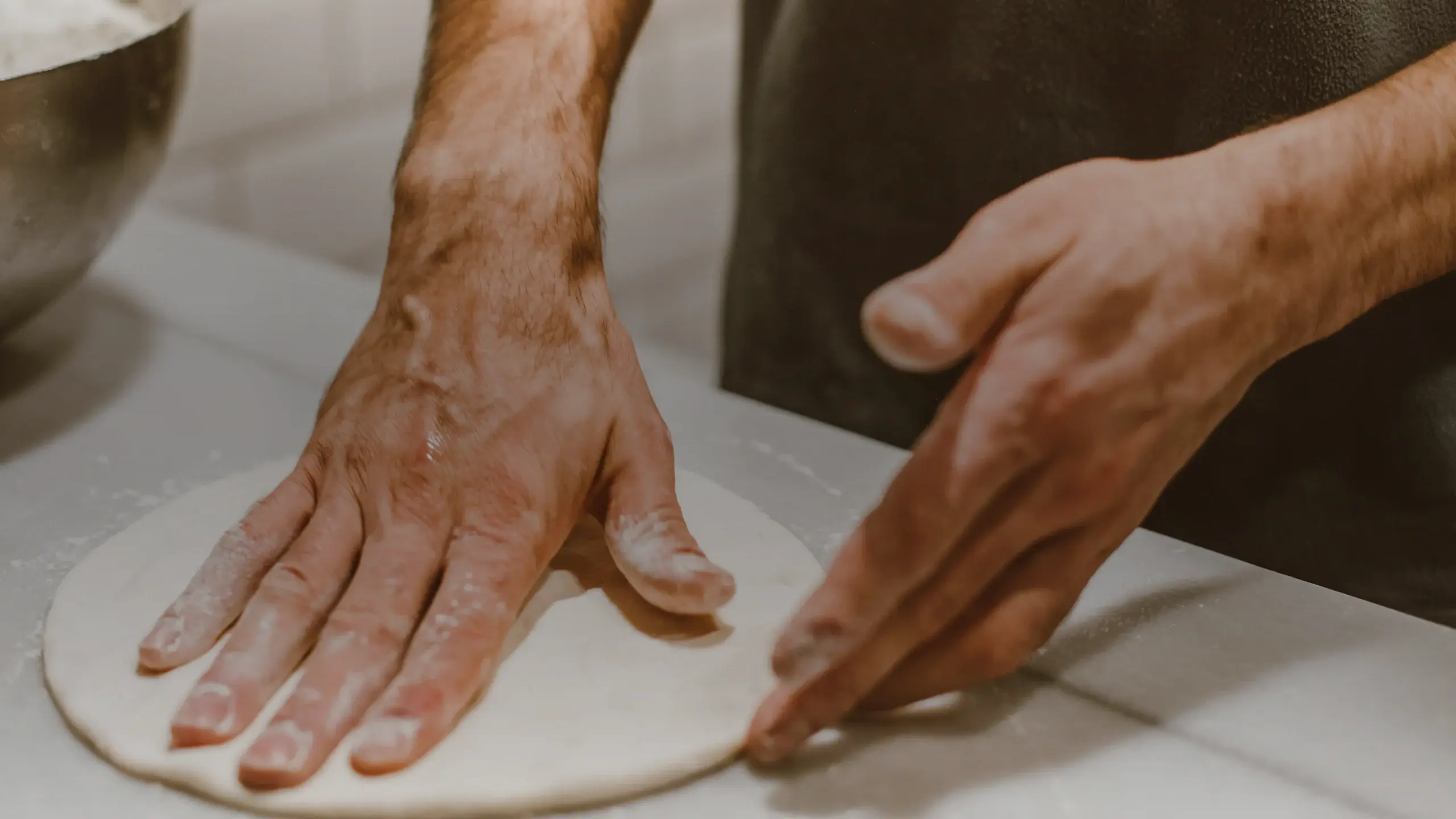 Mains qui étalent un pâton de pizza sur un plan fariné