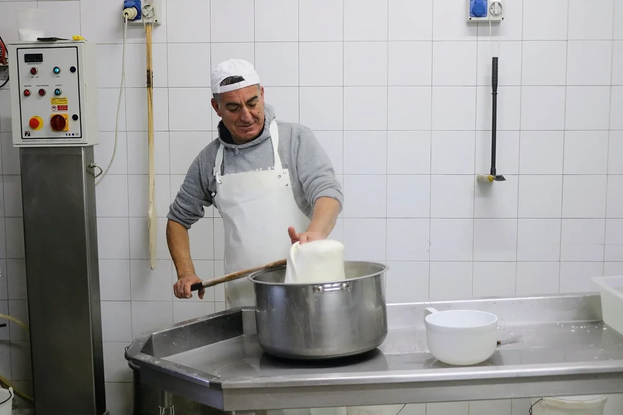 Fromager étirant la pâte de mozzarella au-dessus d'une cuve d'eau chaude