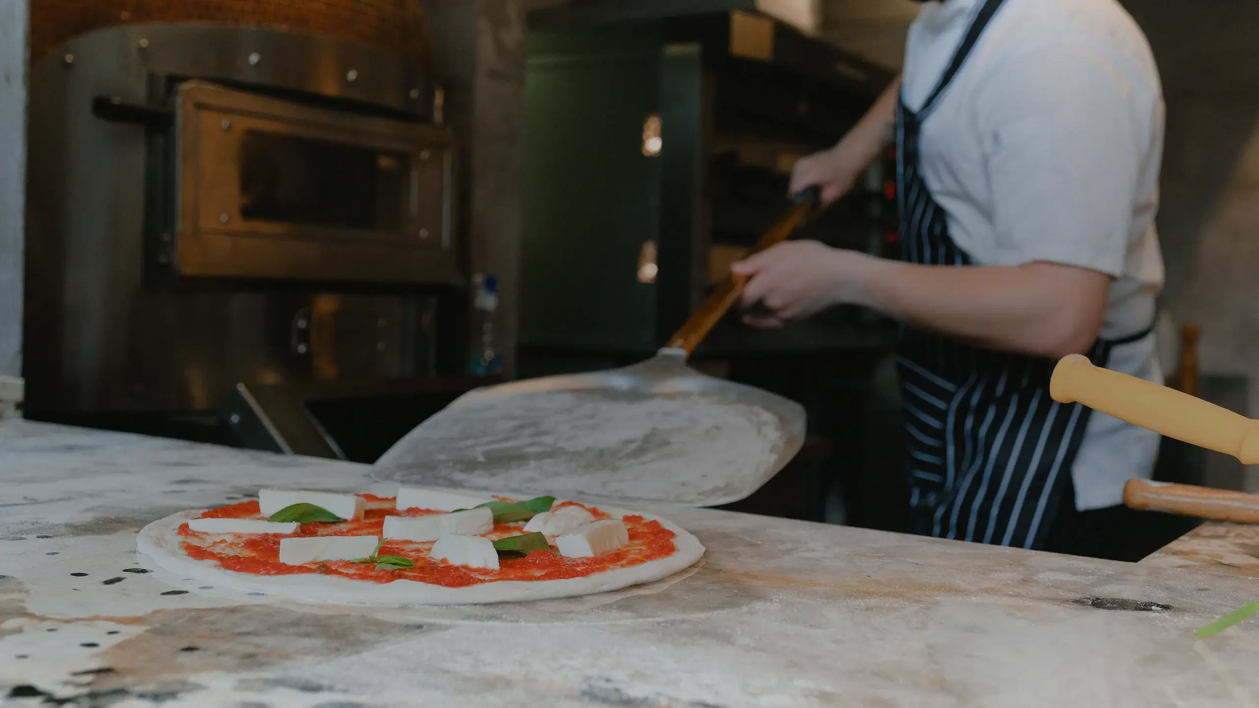 Une pizza napolitaine en cours de garniture devant le four à bois