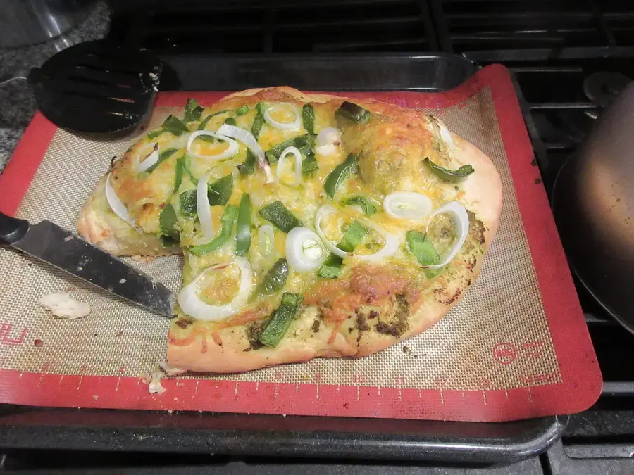 Pizza maison sortie du four, garnie de poivron vert et d'oignon, posée sur un tapis de cuisson