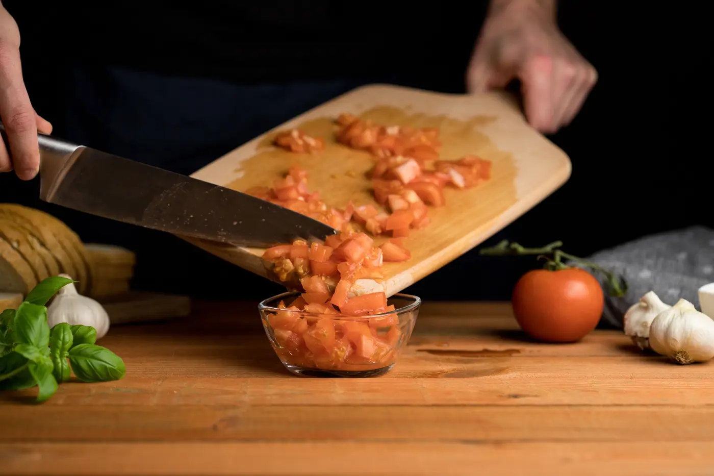 Tomates fraîches coupées en dés au couteau, versées d'une planche dans un bol en verre